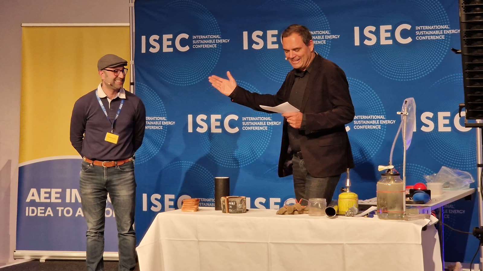 Pakdad Langroudi auf der Bühne beim Science SLAM der ISEC 2026 in Graz, neben einem Tisch mit Demonstrationsaufbauten